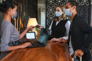couple-and-receptionist-at-counter-in-hotel-wearing-medical-masks-as-picture-id1224155565