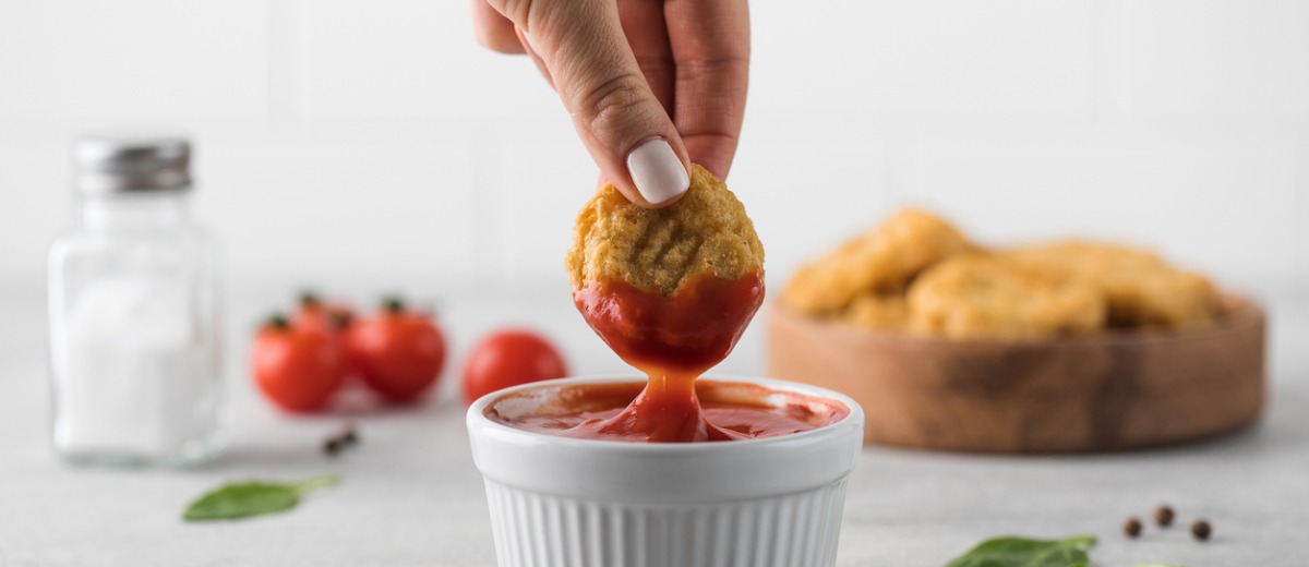 Woman dipping a chicken nugget into a dish filled with ketchup