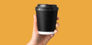 A hand holding a coffee cup with an orange background