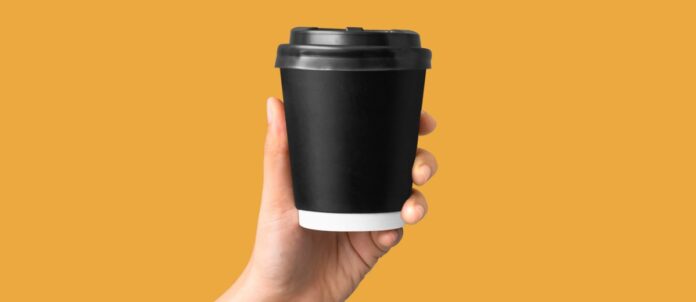 A hand holding a coffee cup with an orange background