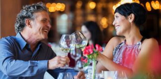 Smiling couple raising toast with white wine at restaurant