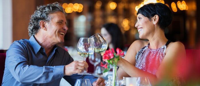Smiling couple raising toast with white wine at restaurant