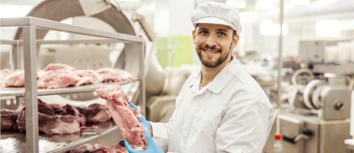 Meat factory worker is holding piece of raw meat