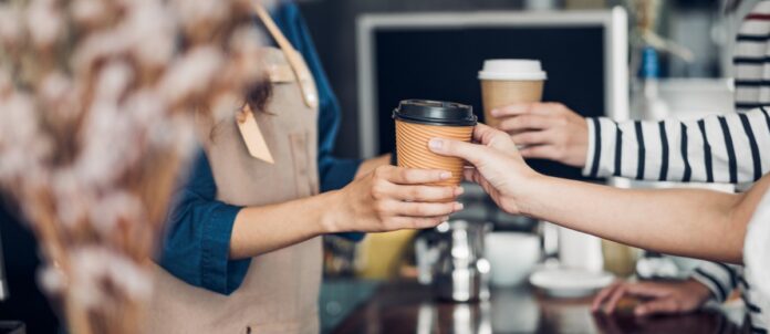 Barista serving cup of coffee to customer at cafe counter