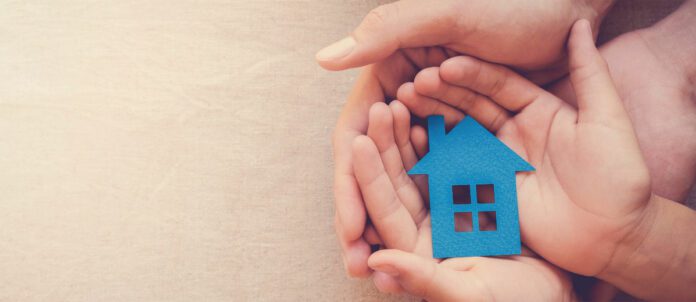 Adult and child hands holding blue paper house for family home