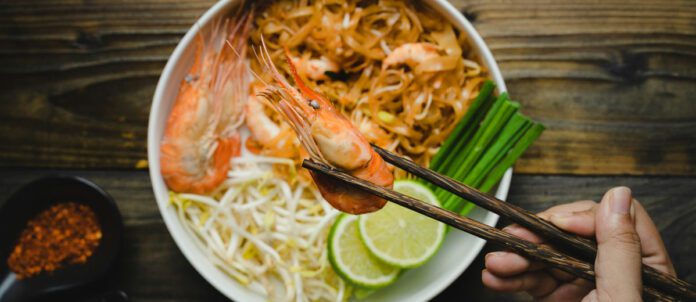 Top view of Pad Thai stir-fried rice noodle with shrimp and scallions on wooden table.