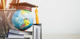 Graduation hat on globe, books with pencils on wood white background