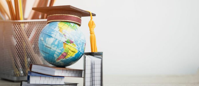 Graduation hat on globe, books with pencils on wood white background