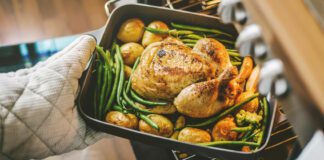 Cook taking ready fried baked chicken with vegetables from the oven