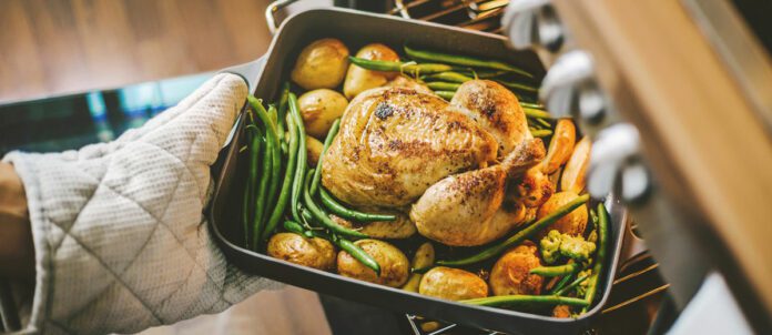 Cook taking ready fried baked chicken with vegetables from the oven