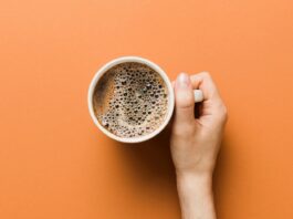 Woman hand holding a cup of coffee on colored background