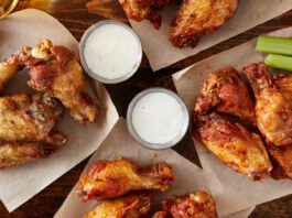 Overhead view of four different flavoured chicken wings with ranch dressing, beer, and celery sticks