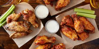 Overhead view of four different flavoured chicken wings with ranch dressing, beer, and celery sticks