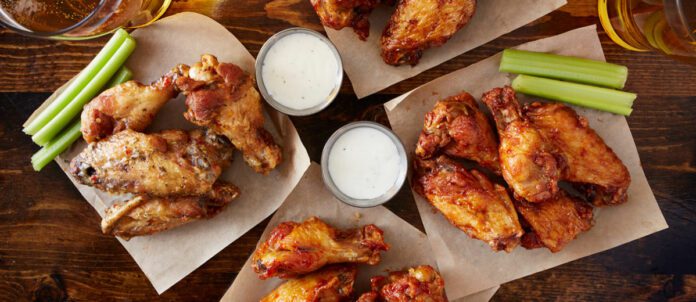 Overhead view of four different flavoured chicken wings with ranch dressing, beer, and celery sticks