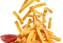 French Fries dropping down onto a plate with ketchup on the side