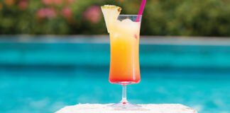 Cocktail in glass with slice on pineapple on side beside pool