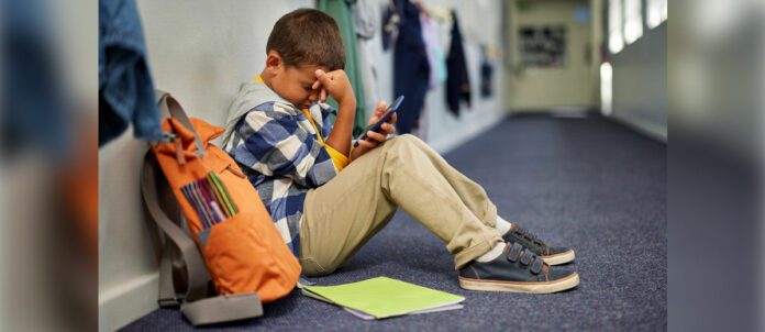 Young child sitting on the floor using smartphone to call for mental health support while at school