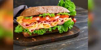 submarine sandwich with ham, cheese, lettuce, tomatoes and microgreens on old wooden dark background
