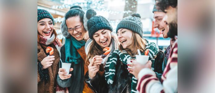 Happy friends having fun and laughing while drinking hot chocolate at winter fair