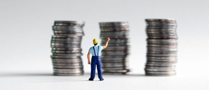 A miniature man reaching for a pile of three coins.