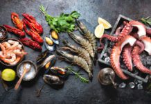 Octopus tentacles, black tiger shrimps, king prawn and mussels with fresh herbs and seasoning on black rustic background