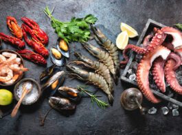 Octopus tentacles, black tiger shrimps, king prawn and mussels with fresh herbs and seasoning on black rustic background