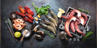Octopus tentacles, black tiger shrimps, king prawn and mussels with fresh herbs and seasoning on black rustic background