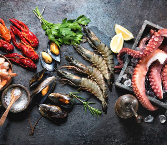 Octopus tentacles, black tiger shrimps, king prawn and mussels with fresh herbs and seasoning on black rustic background