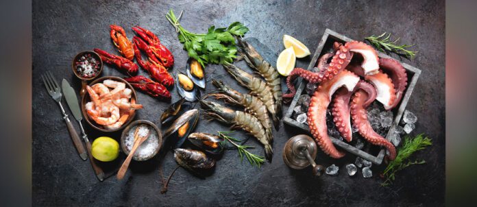 Octopus tentacles, black tiger shrimps, king prawn and mussels with fresh herbs and seasoning on black rustic background